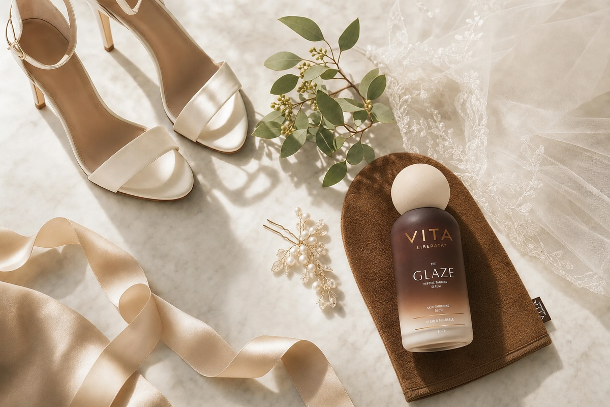 Glaze Untinted self tan for weddings. Elegant wedding-prep flat lay with silk ribbon, pearl hairpin, ivory heels, veil edge, greenery and a tanning mitt on marble in soft light.
